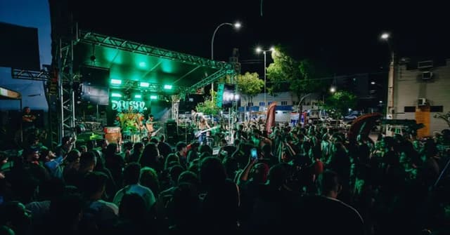 Show ao ar livre à noite, com plateia diante de um palco iluminado de verde e o painel do DoSol ao fundo