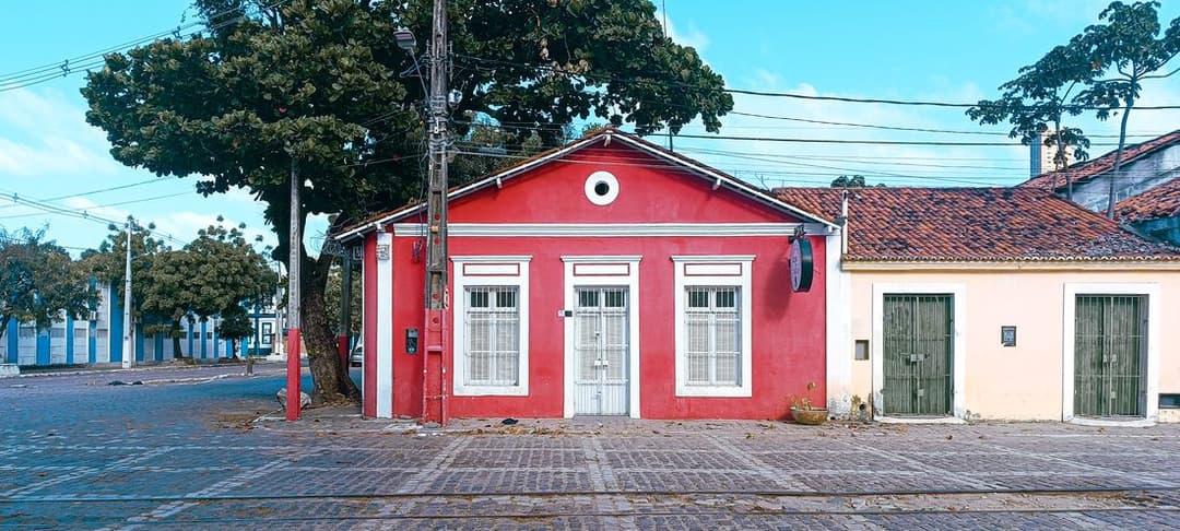 Casa térrea vermelha de esquina numa rua de paralelepípedos da Ribeira, em Natal, ao lado de uma casa amarela de portas de ferro