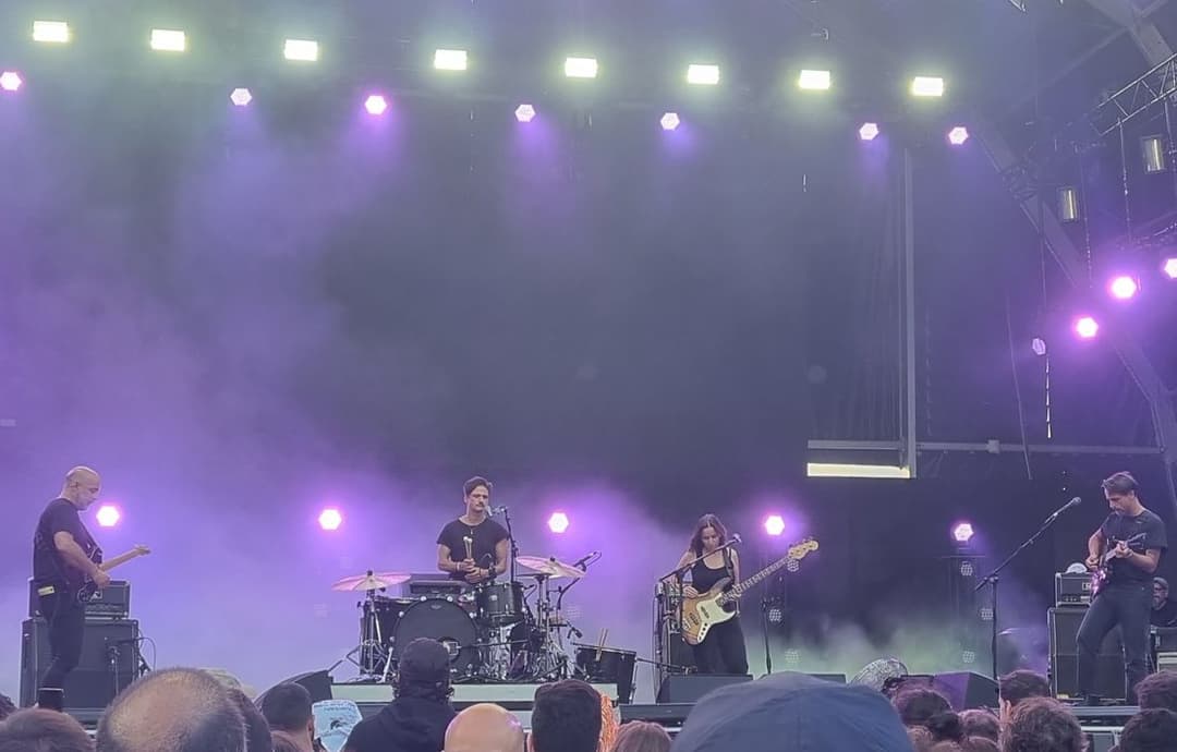 O Linda Martini, com bateria, baixo e duas guitarras, num palco grande sob luzes roxas e fumaça