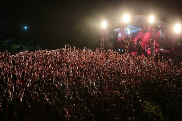 Multidão de braços erguidos diante de um palco iluminado à noite, no Festival DoSol 2017