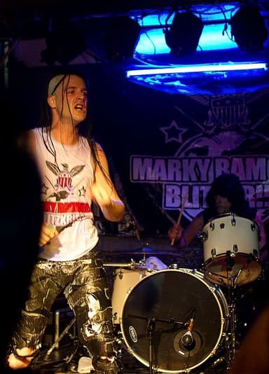 Michale Graves canta de regata branca em primeiro plano; atrás dele, Marky Ramone toca bateria diante do painel do Marky Ramone's Blitzkrieg