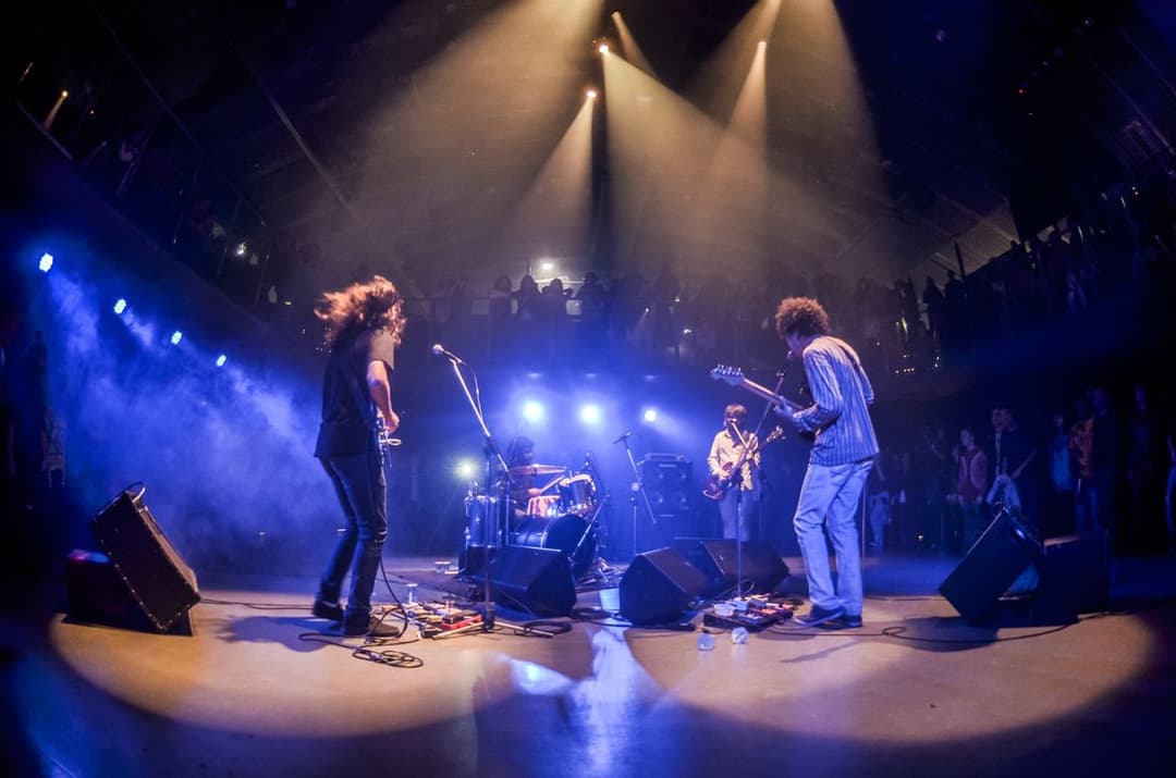 Quatro músicos tocam num palco escuro cortado por feixes de luz azul