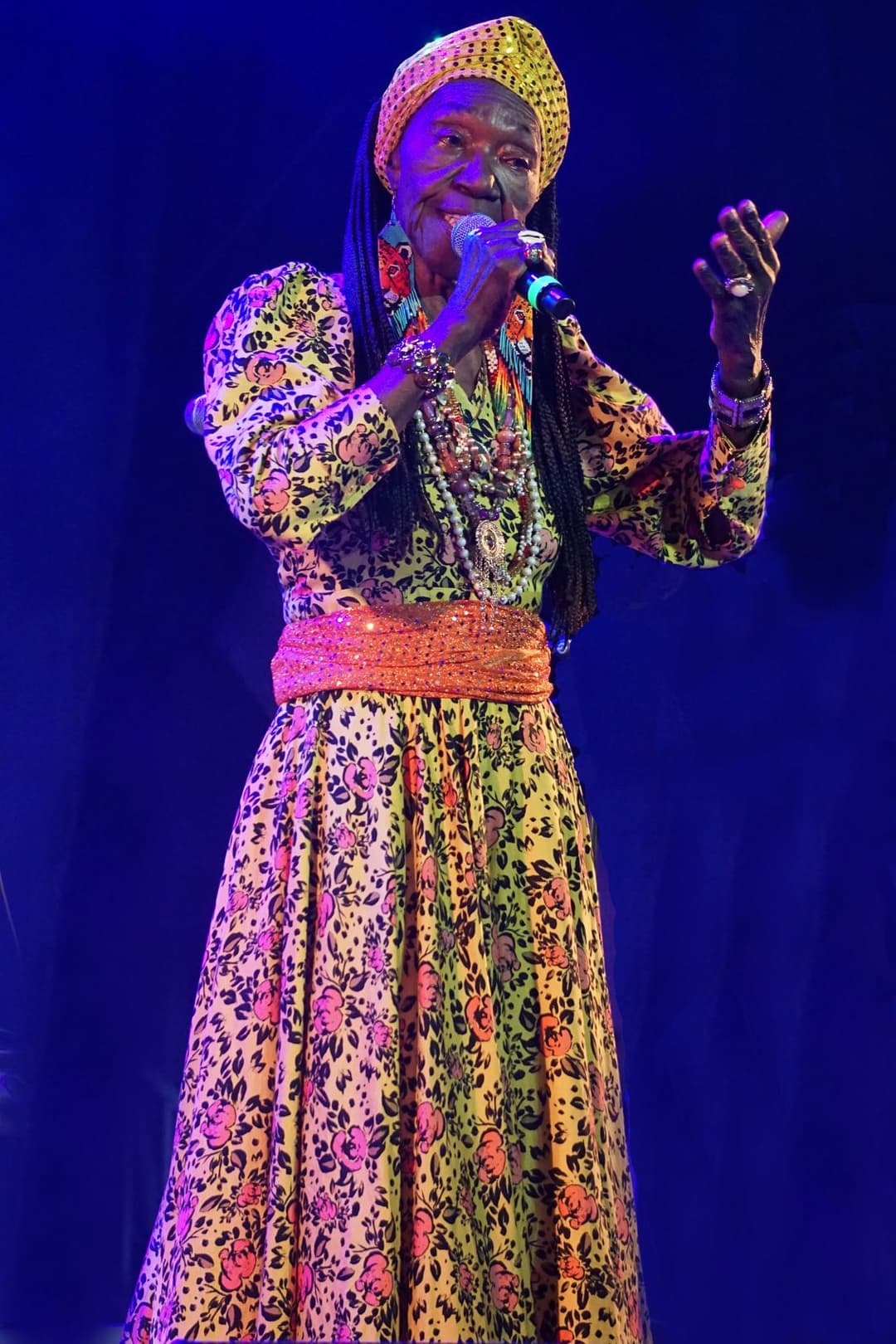 Cantora de turbante e vestido estampado canta ao microfone sob luz azul