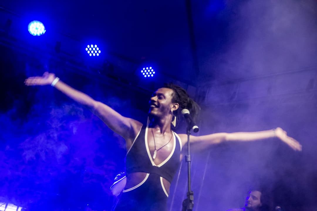 Liniker canta de braços abertos no palco, sob luz azul