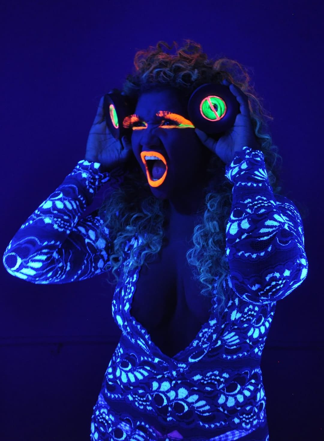 Gaby Amarantos com maquiagem fluorescente sob luz negra, as mãos na cabeça