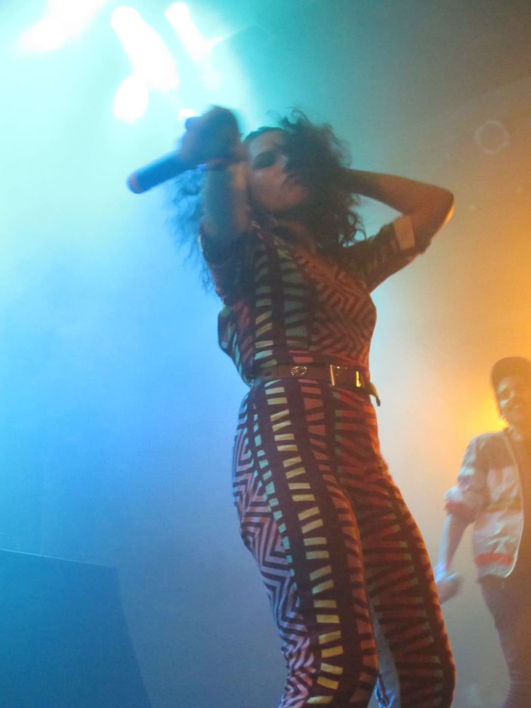 A vocalista da Banda Uó canta de macacão estampado, sob luz verde e laranja