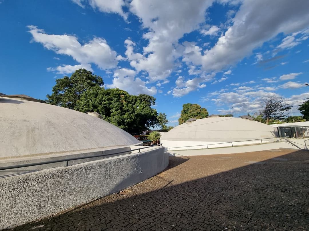 Pátio aberto com duas cúpulas brancas baixas, árvores e céu azul com nuvens