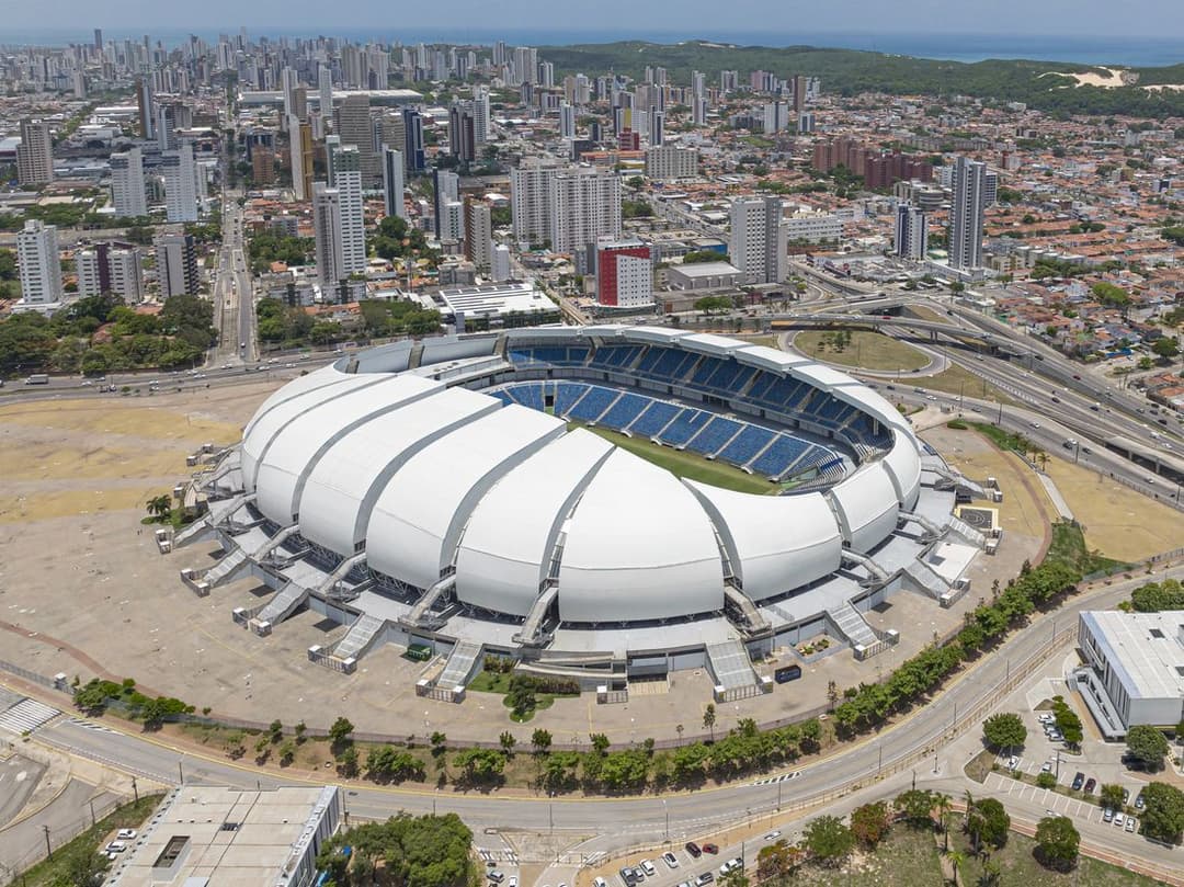 Vista aérea da Arena das Dunas, um estádio de cobertura branca em gomos, cercado por avenidas e prédios de Natal