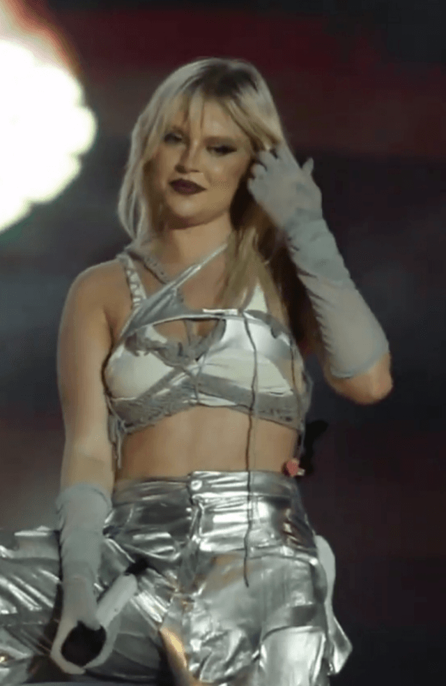 Luísa Sonza, loira, de top e calça prateados e luvas cinza, num palco