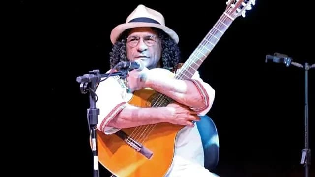 Genésio Tocantins, de chapéu, abraçado ao violão no palco