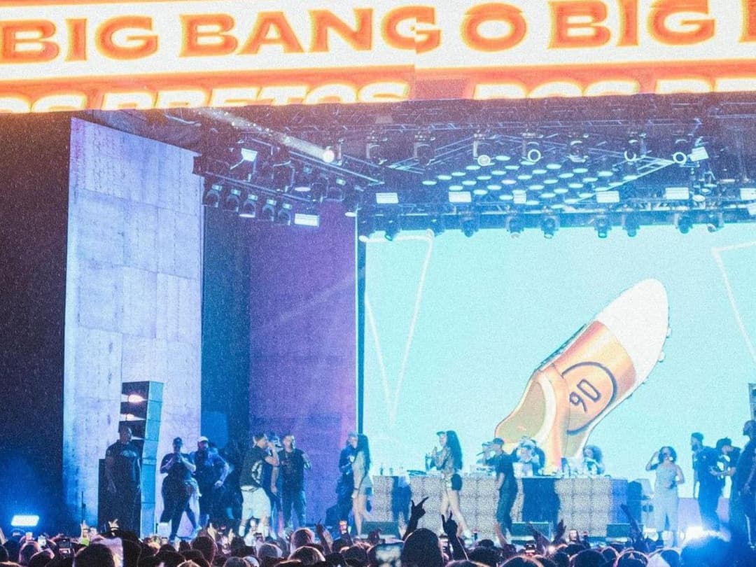 Palco com o letreiro de LED O Big Bang dos Pretos, cantores e DJs sob chuva fina e o público de braços erguidos