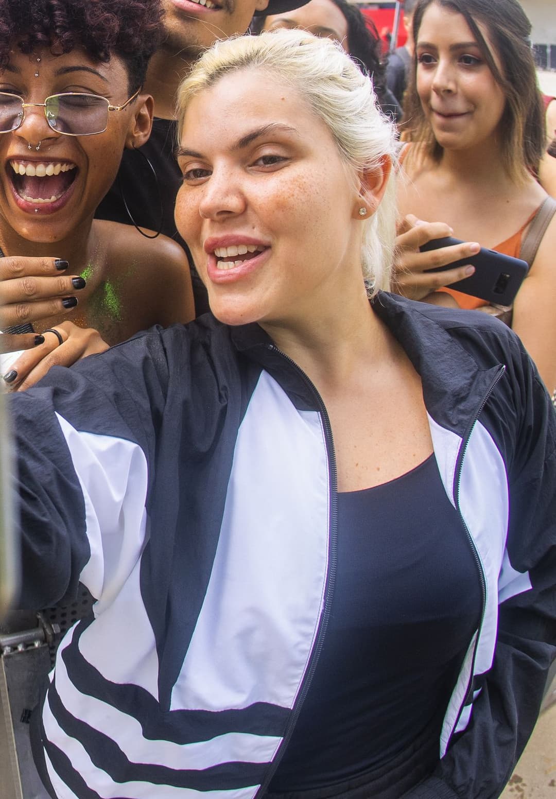 Duda Beat, de cabelo platinado e jaqueta preta e branca, sorri entre fãs